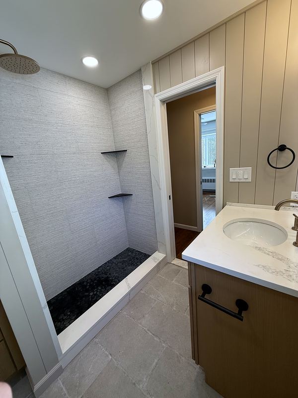 Walk-in shower with large-format tile beside a wood vanity