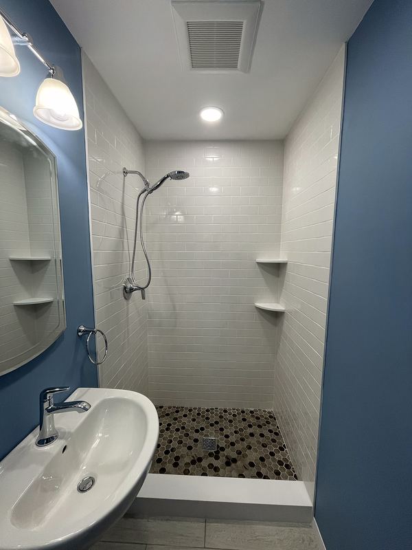 White tile shower with pebble floor and blue accent wall
