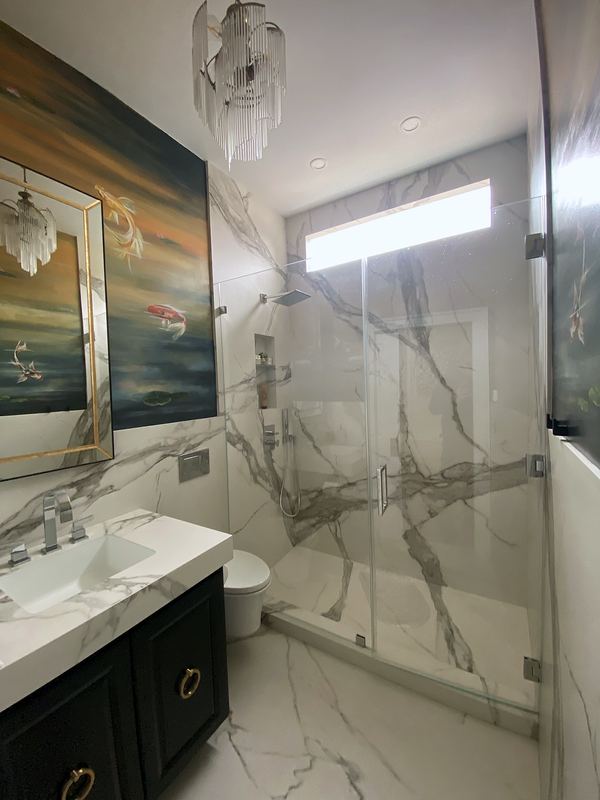 Marble-look porcelain shower with frameless glass and navy vanity