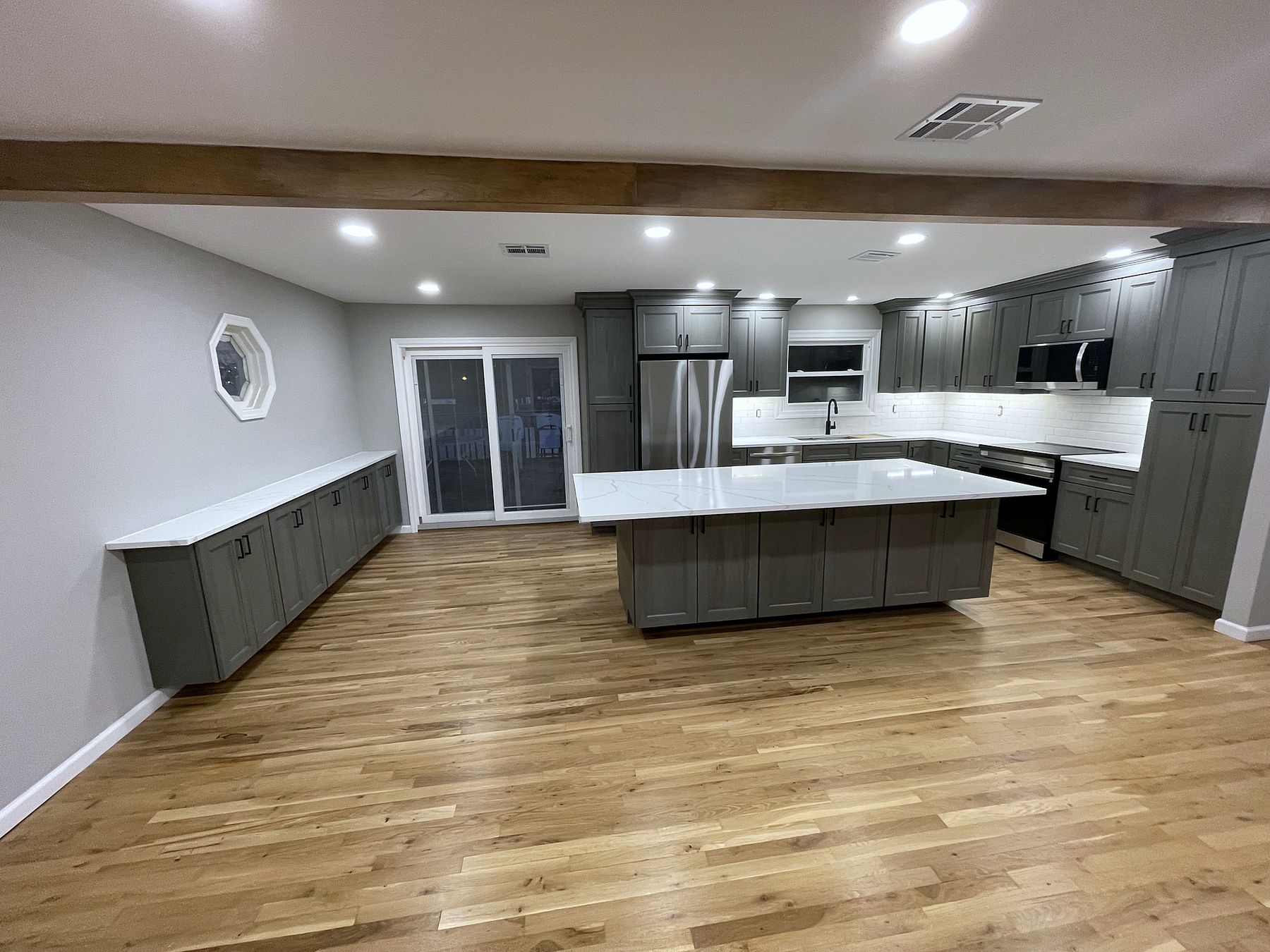 Open kitchen remodel with gray shaker cabinets, white quartz island and wide-plank oak floors